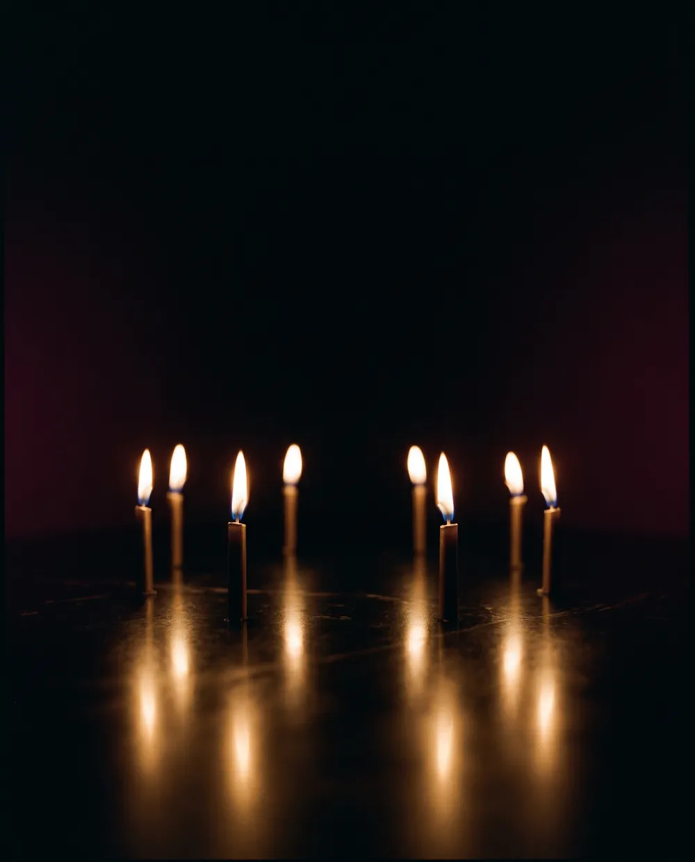 Eight candle flames in a ring on dark stone, their reflections drawing toward the camera
