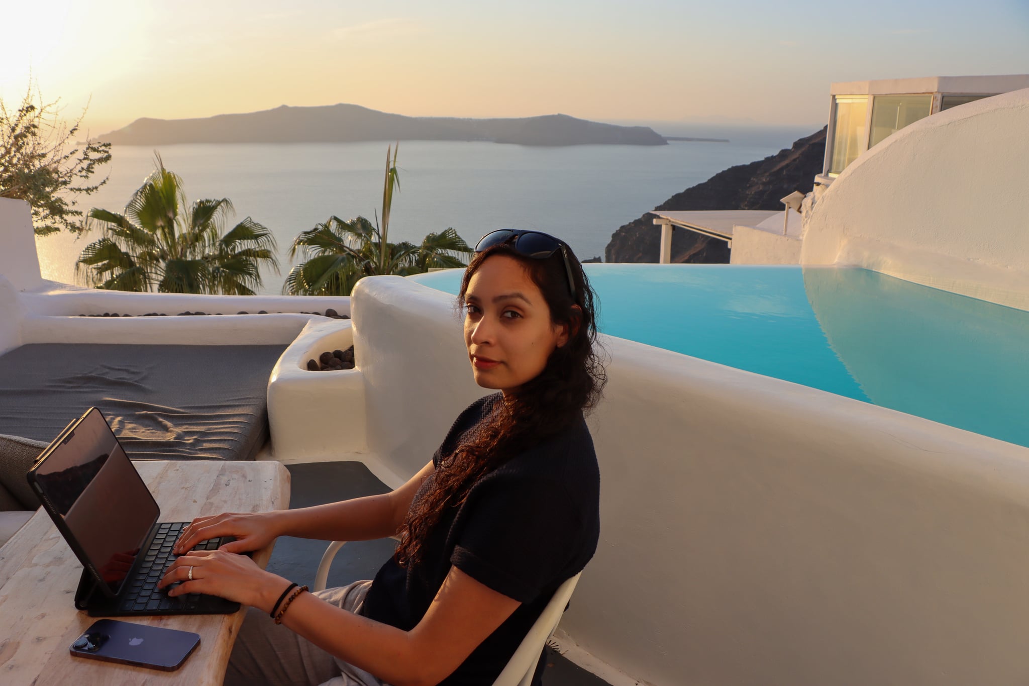 Mel Cobian working on a laptop on a terrace above the sea in Santorini